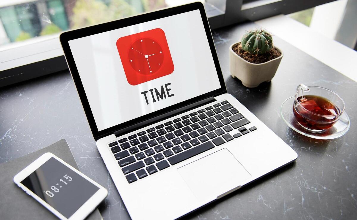 Laptop displaying "TIME", with a phone, cactus, and tea on a modern desk.