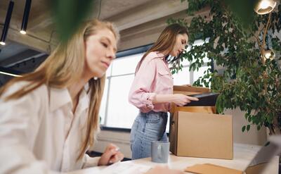 Young businesswoman holding box of personal belongings about to leave office after quitting job