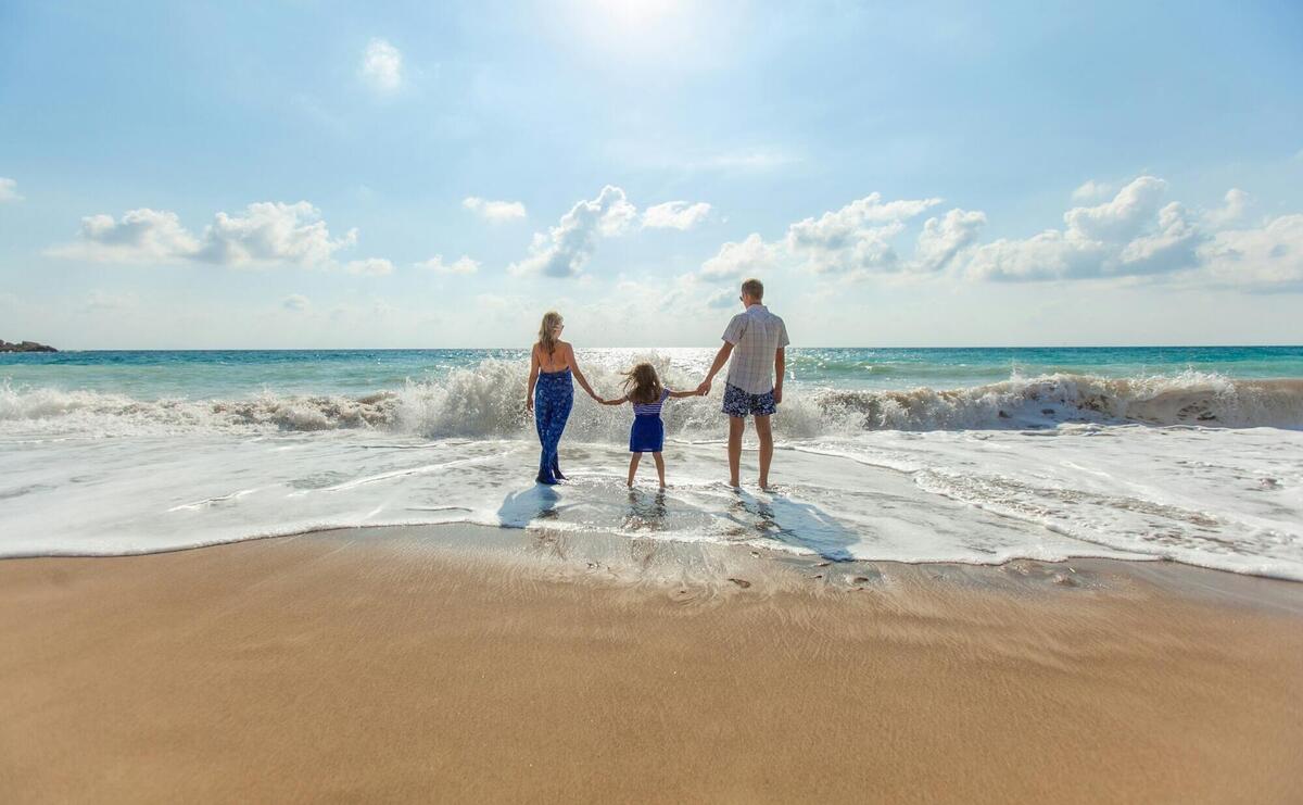 man, woman and child holding hands on seashore