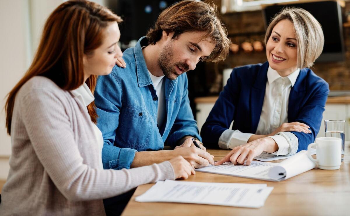 Young couple signing lease agreement while having meeting with real estate agent Focus is on man