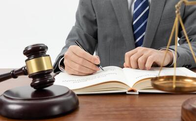 Closeup shot of a person writing in a book with a gavel on the table