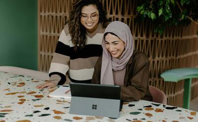 Two women sitting at a table with a laptop