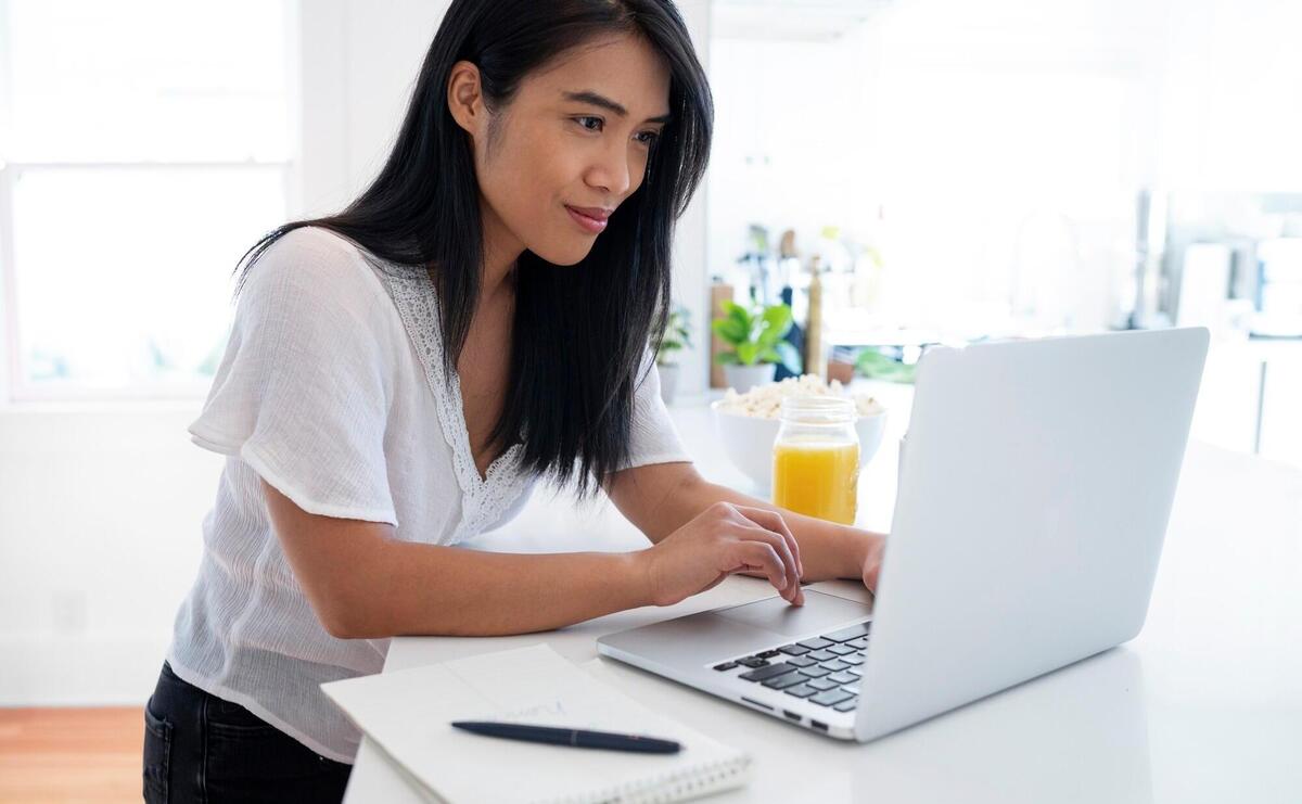 Young woman using laptop and notebook with pen for notes