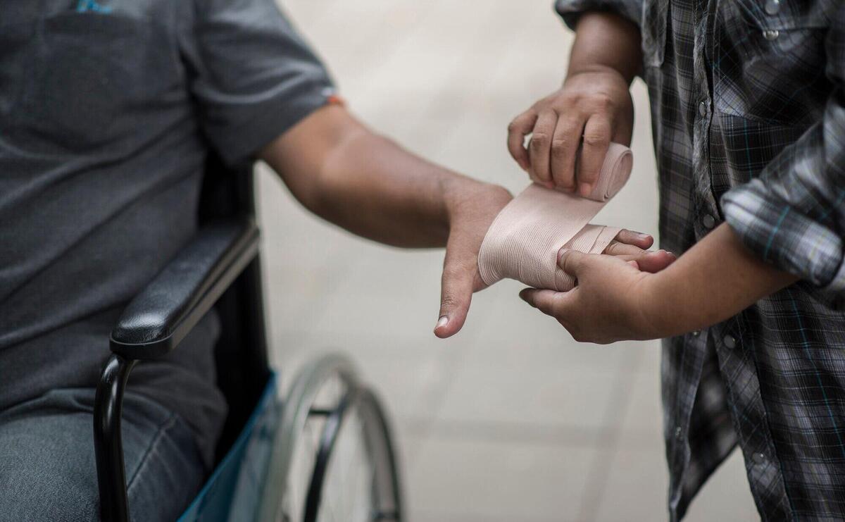 Women are wrapping hands on men sitting on wheelchair patients with bandages.