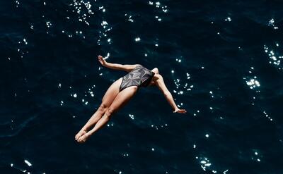 A woman in swimwear fearlessly dives into the deep blue ocean, showcasing grace and freedom.