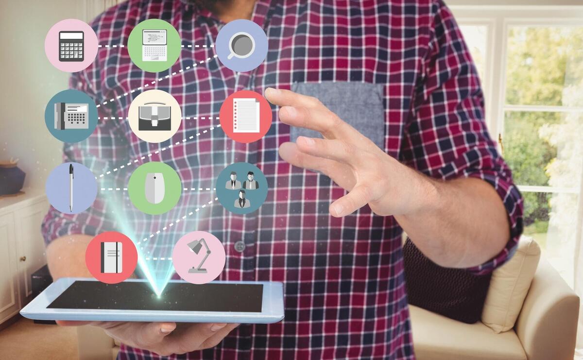 Man holding tablet with digital icons floating, in a cozy home setting.