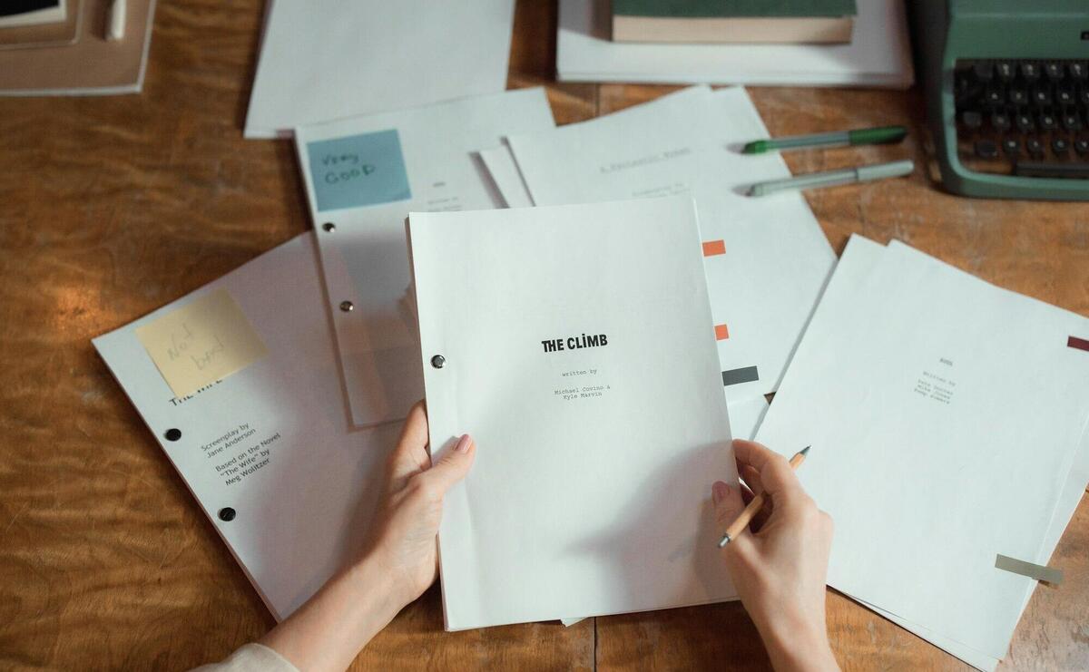 Close-up of hands holding script pages on a wooden desk with a typewriter.