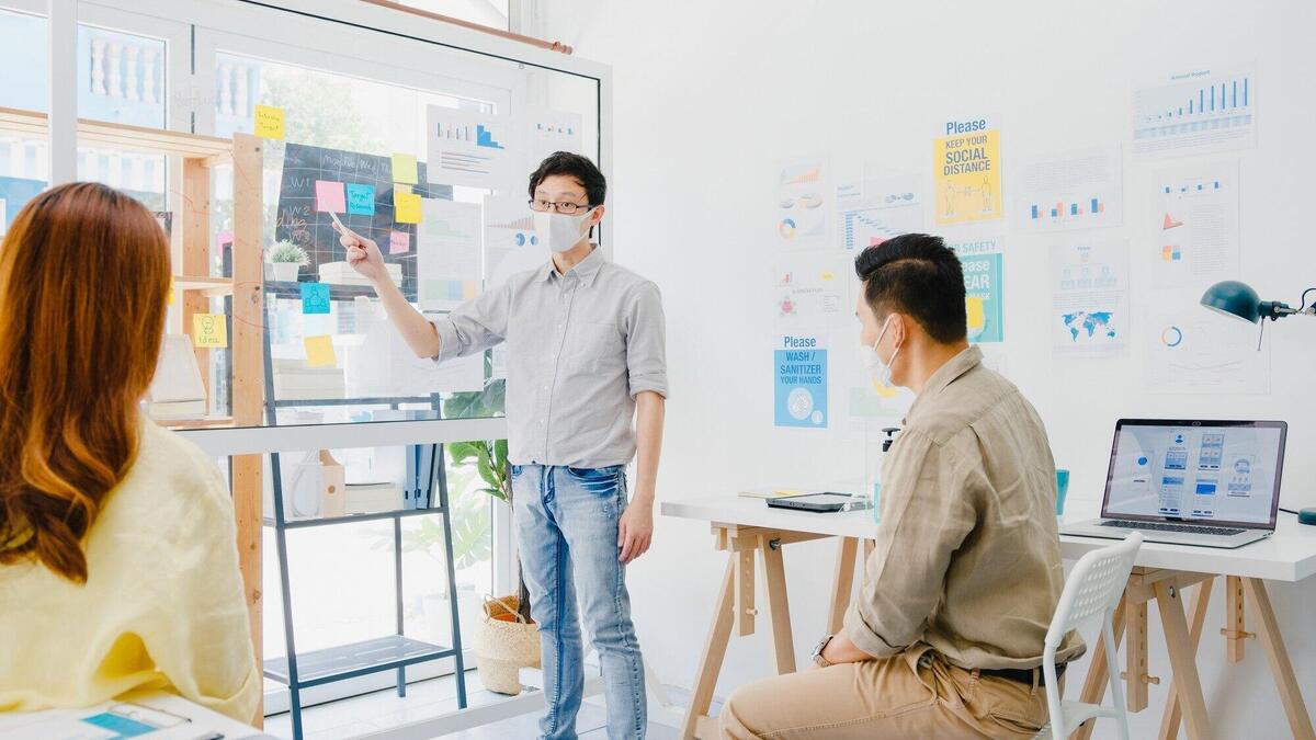 Asia businesspeople meeting brainstorming ideas conducting business presentation ideas project colleagues and wear protective face mask back in new normal office. Lifestyle and work after coronavirus.