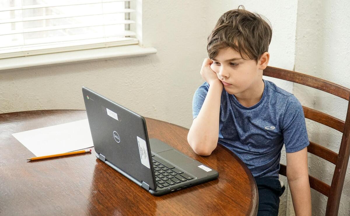 boy in blue crew neck t-shirt using macbook pro on brown wooden table