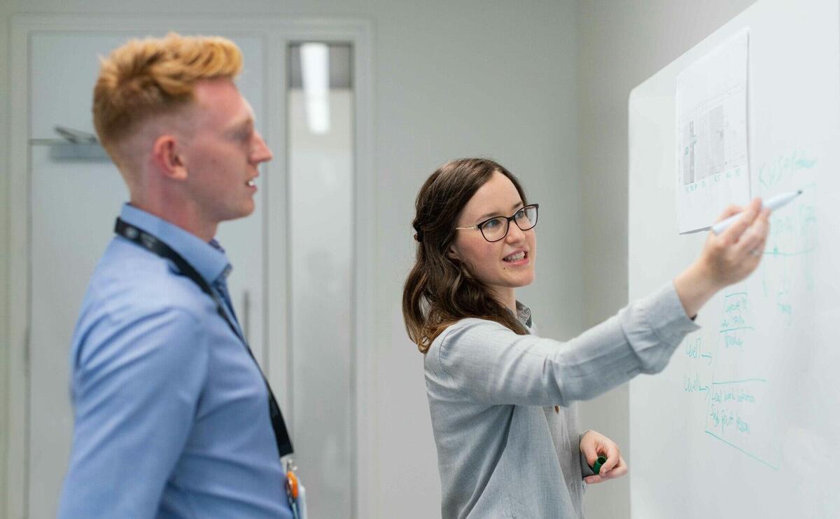 Two colleagues engaged in an office discussion at the whiteboard.