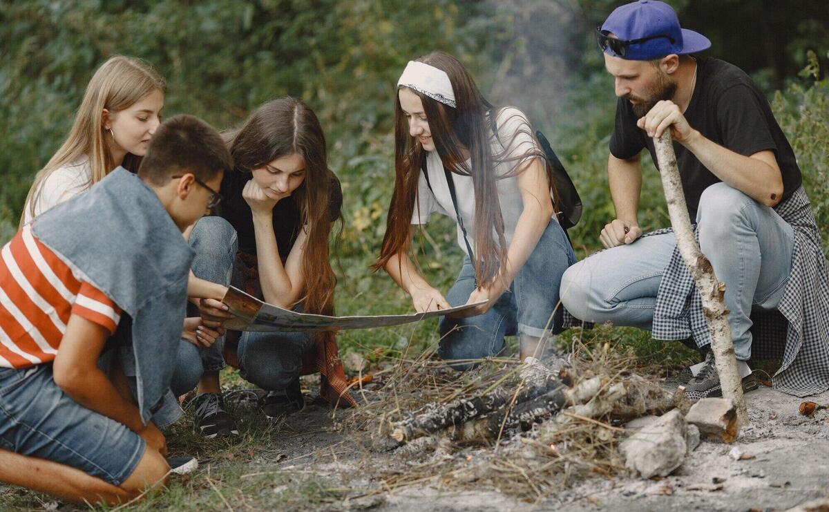 Adventure, travel, tourism, hike and people concept. Group of smiling friends in a forest. People sitting near bonfire.