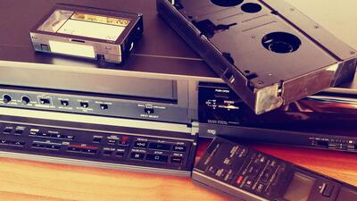 An image of a VHS tape and an audio tape stacked upon a VCR, serving as a visual representation of the topic of digitizing your media collection.