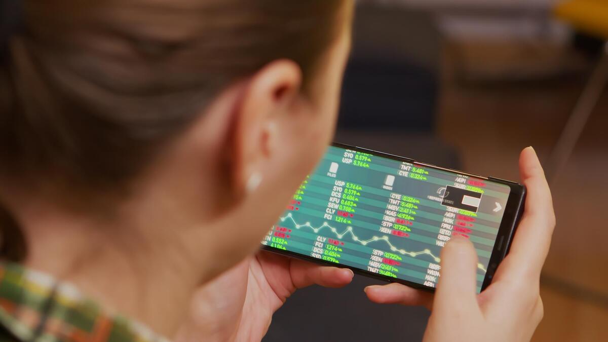 Back view of woman checking stock trading using smartphone.