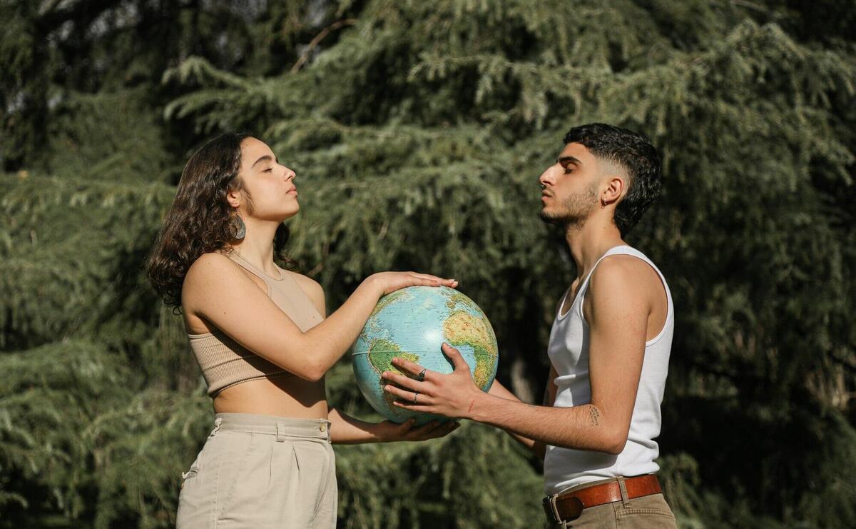 A young couple holds a globe outdoors, symbolizing unity and cooperation.