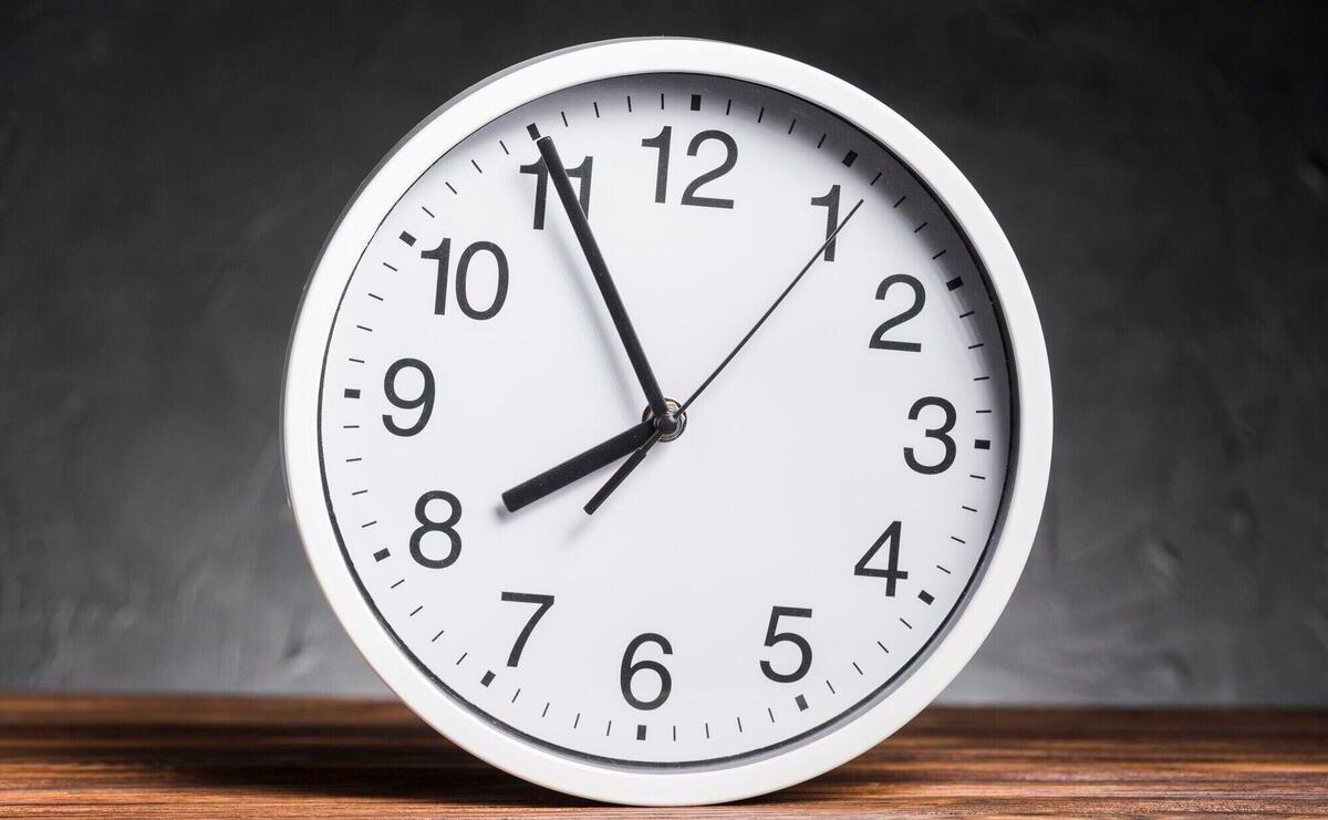 White clock on wooden desk against black background