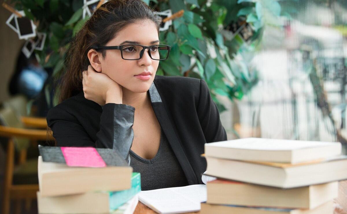Serious female student sitting at table with books