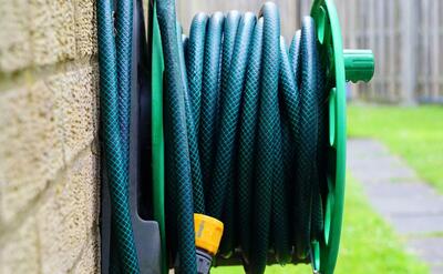 A neatly coiled garden hose on a wall-mounted reel against a brick wall.