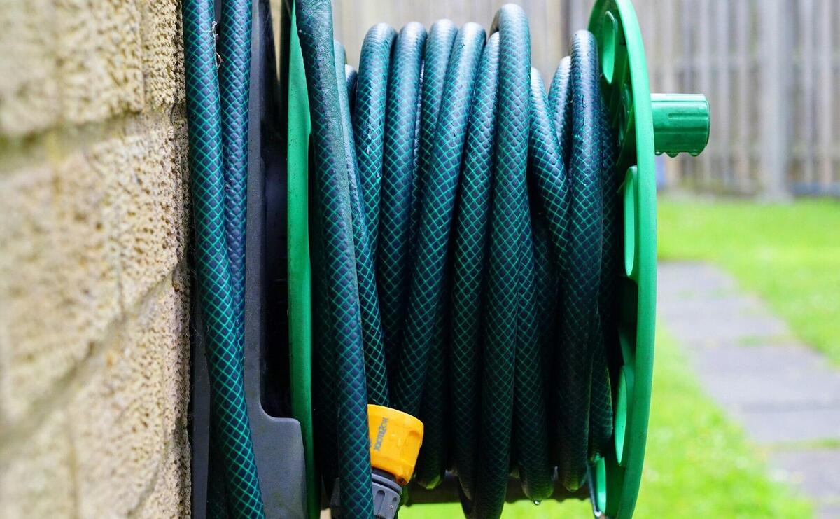 A neatly coiled garden hose on a wall-mounted reel against a brick wall.