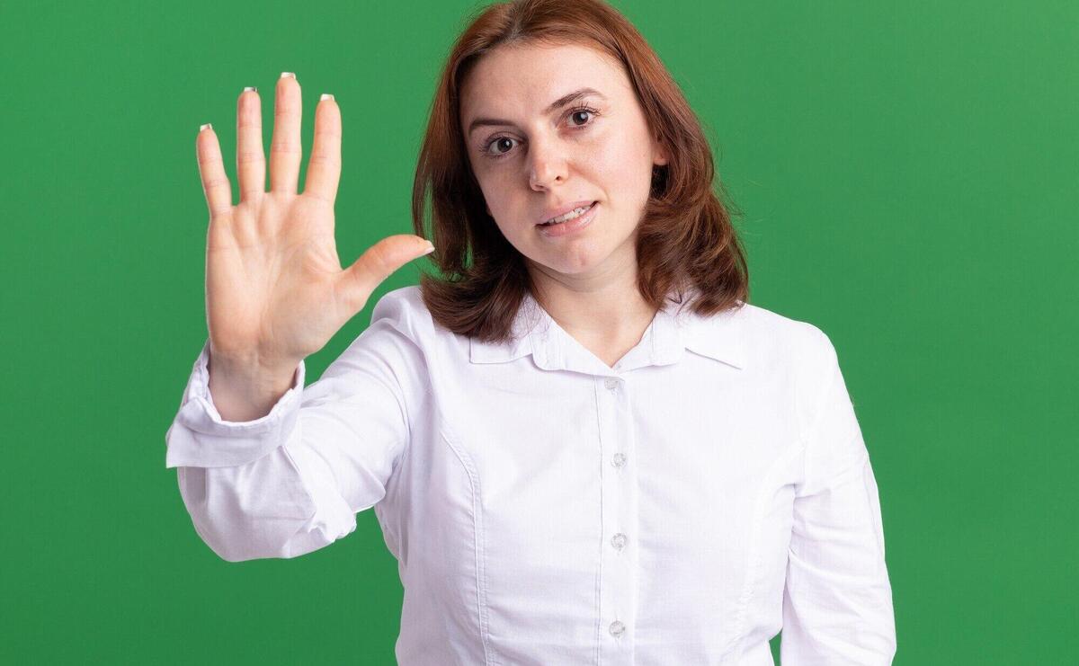 Young woman in white shirt looking at front showing and pointing up with fingers number five smiling anding over green wall