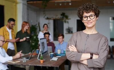 Smiling businesswoman with curly hair stands confidently in a modern office space with colleagues.