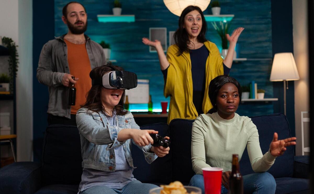 Happy gamer woman with virtual reality headset winning online competition playing videogames using gaming joystick enjoying victory with friends at home. Concept of multu-ethnic friends hanging out