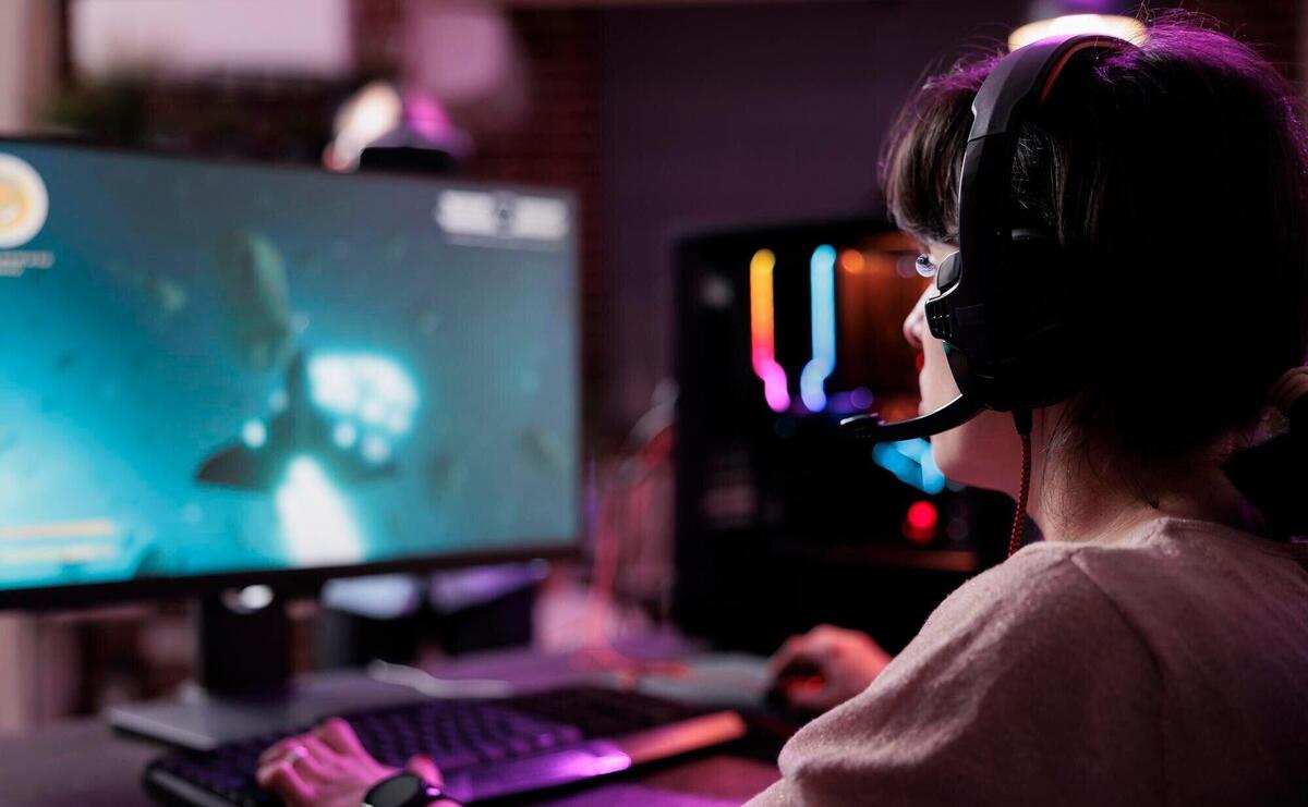 Young streamer playing video games online on live stream, using computer and neon lights in living room. Female gamer having fun with action gameplay on virtual shooting tournament.