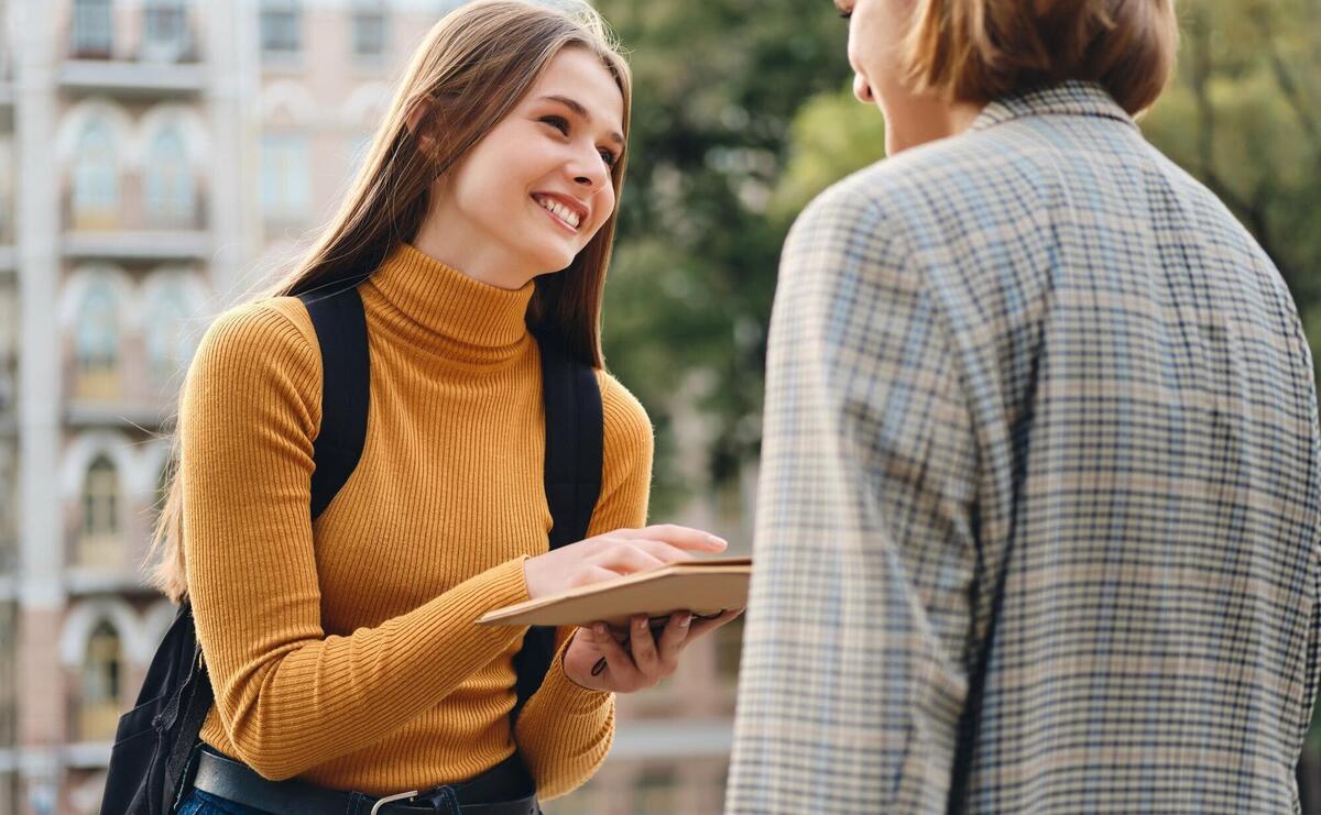 Attractive cheerful casual student girl happily talking with friend during study break outdoor