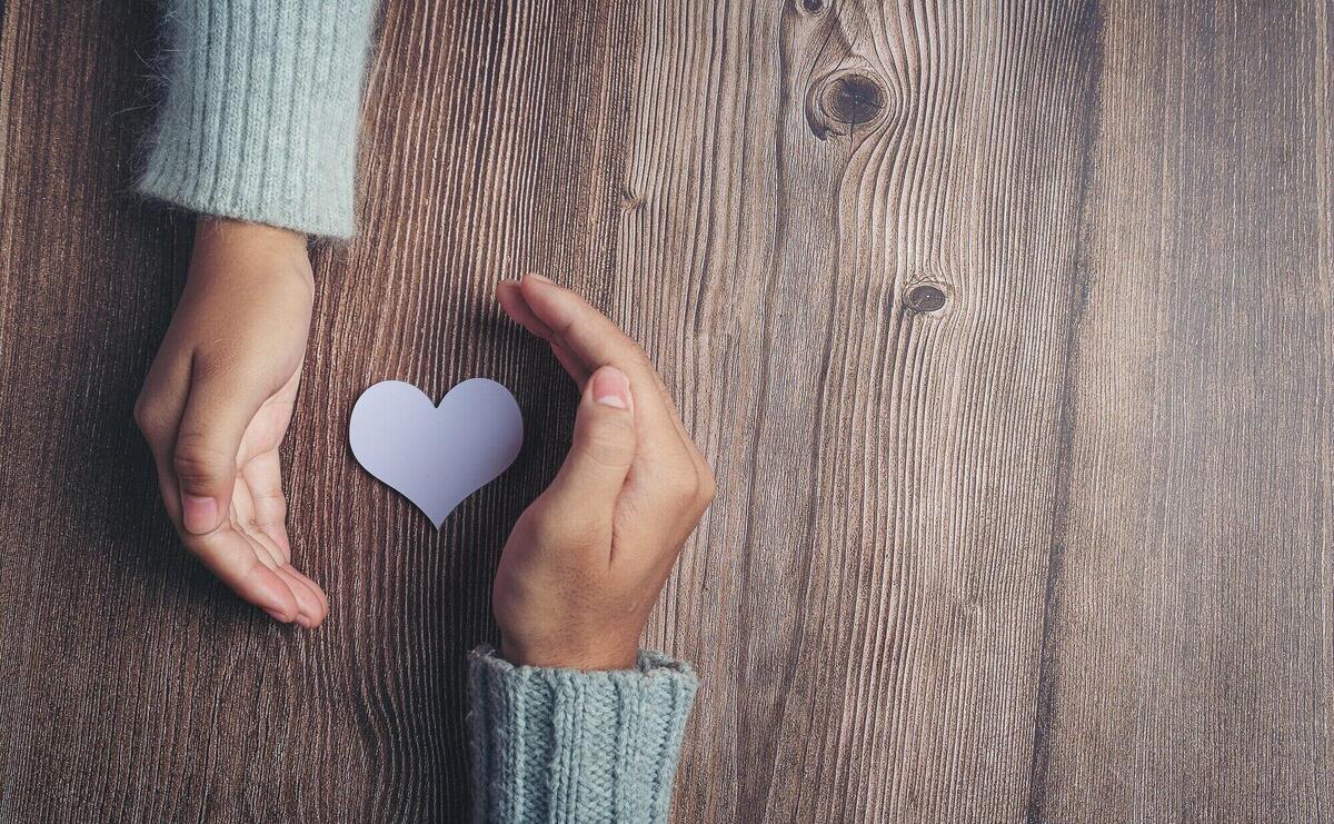 Paper heart and couple's hands on wooden table