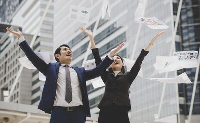 Business people are throwing up papers, while standing in front of office building. Business successfully concept.