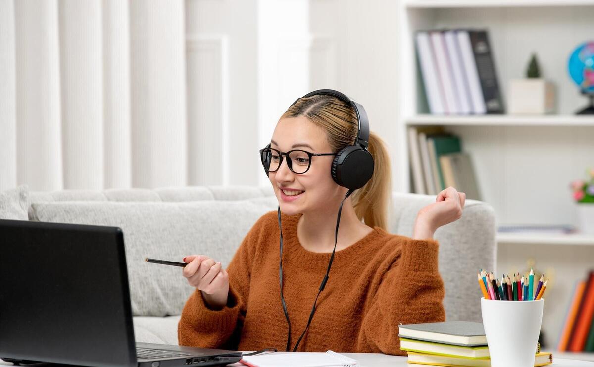 Student online cute girl in glasses and sweater studying on computer smiling happily