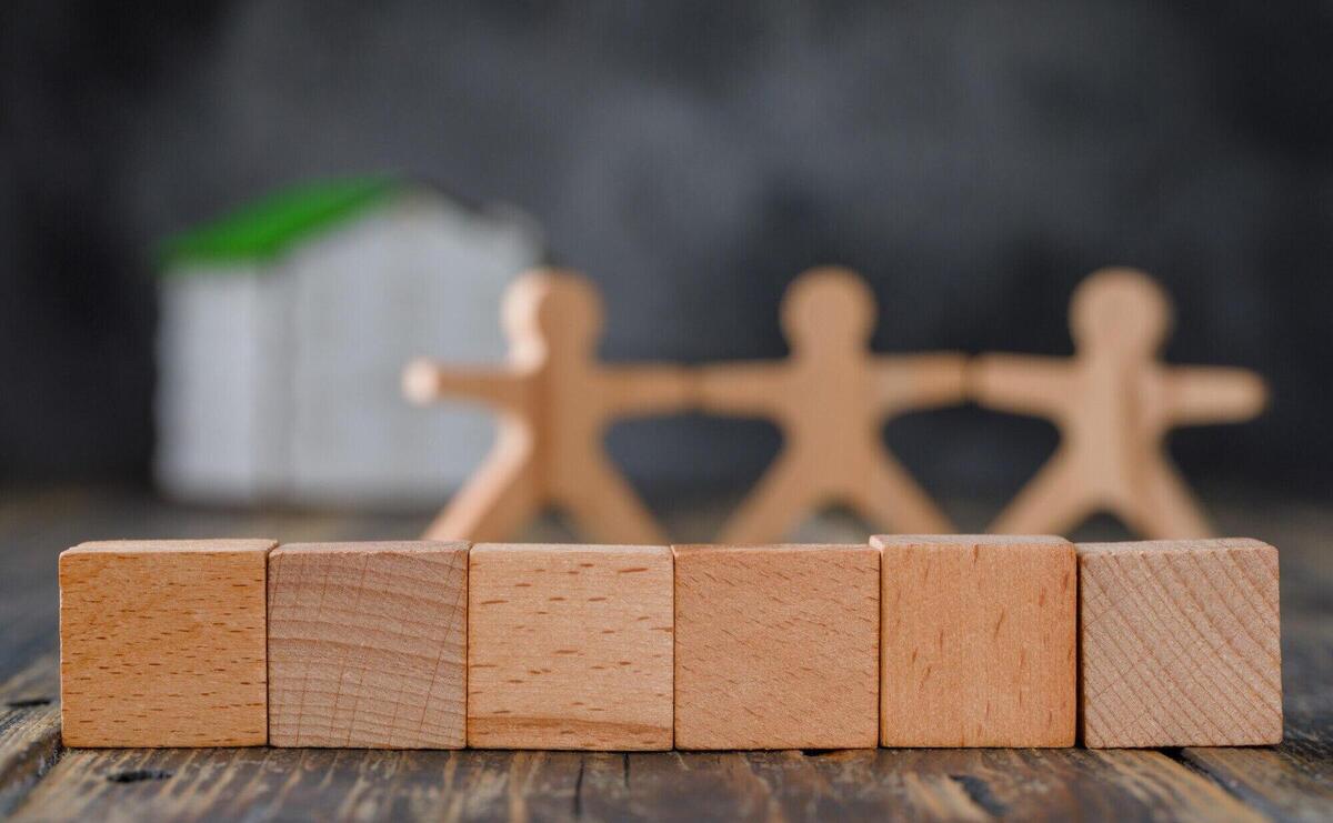 Family safety concept with wooden figures of people, cubes, model house side view.