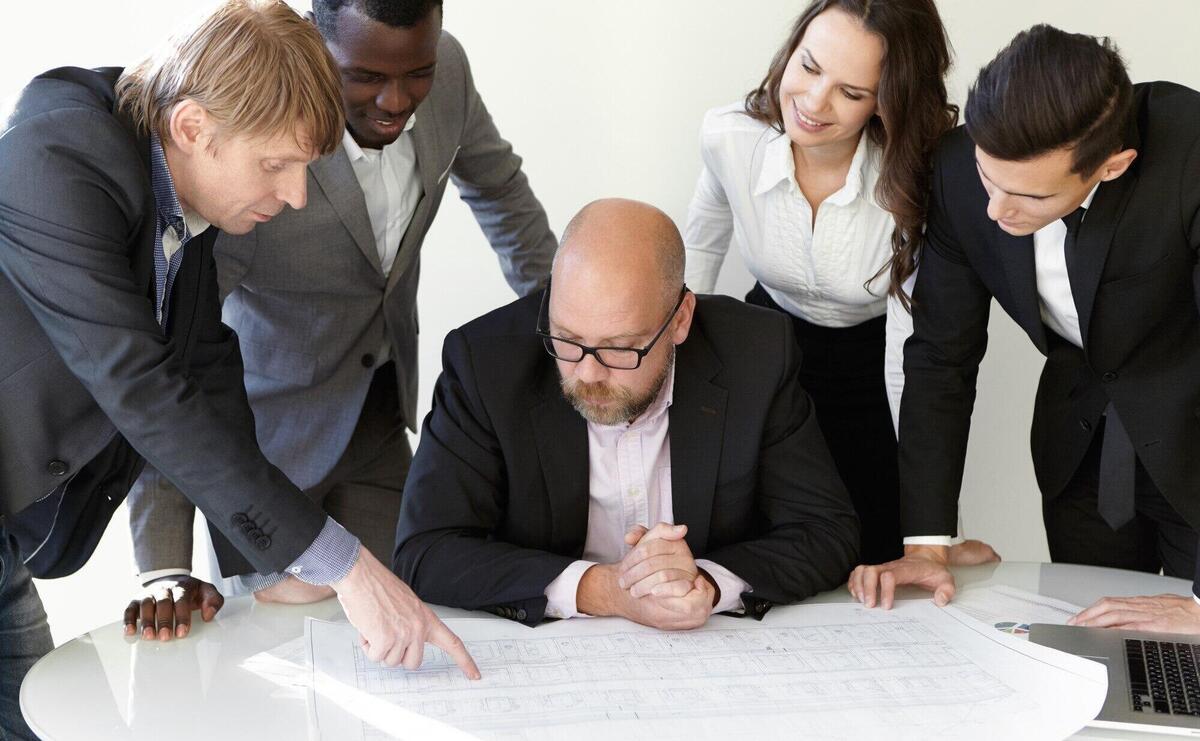 Productive teamwork at office. the main engineer in spectacles listening to new ideas of his colleague. caucasian man pointing finger at schematic drawings. coworkers approving his offer with smile.