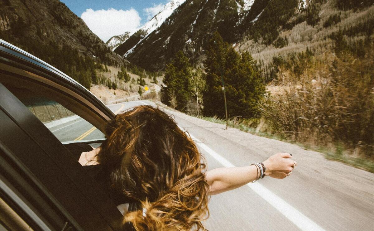 woman riding on vehicle putting her head and right arm outside the window while travelling the road