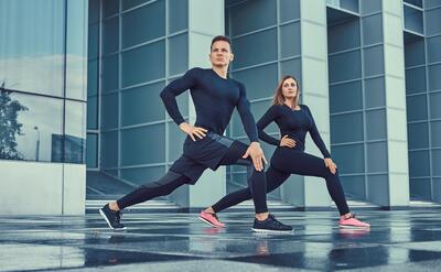 Young fitness couple in a sportswear, doing a lunges in the modern city against a skyscraper. Healthy lifestyle concept.