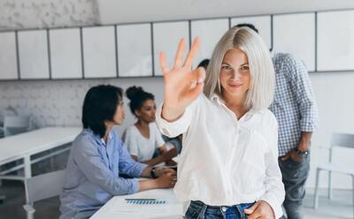 Slim woman with blonde short hair showing okay sign after succesful negotiation. Portrait of asian office worker posing with african colleague during conference with fair-haired woman.