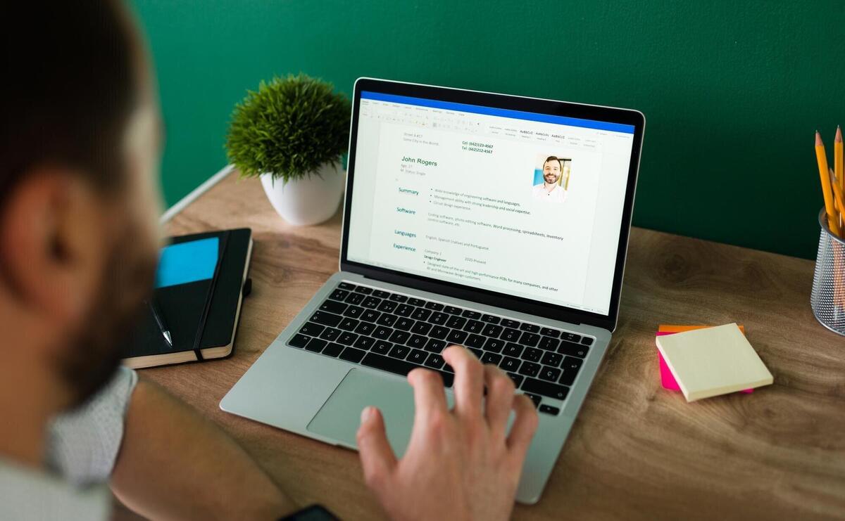 Rear view of an adult man searching for a new job and working on writing his resume on the laptop