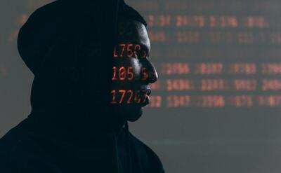 Side profile of a man in a hoodie, surrounded by red code, depicting cybersecurity theme.