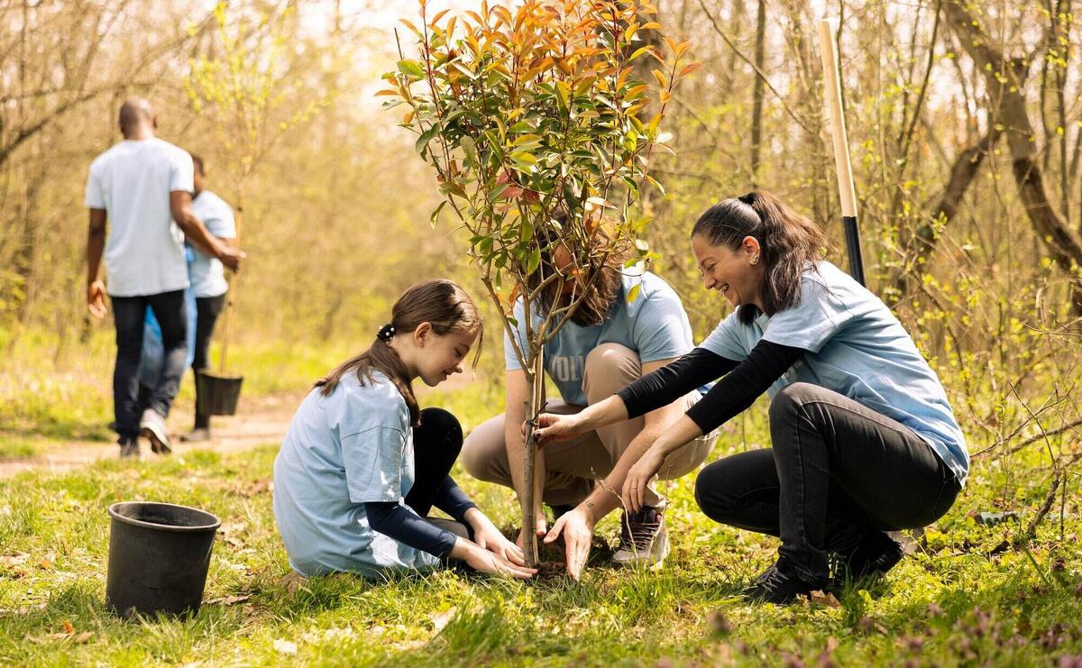 Volunteers and a little kid planting tree and covering hole in the ground