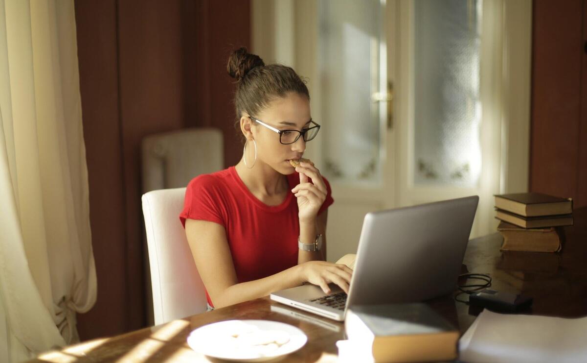 Young attractive female student eating cookies and working with a laptop