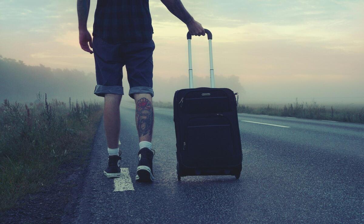 Man walking with a suitcase along a foggy road at sunrise, symbolizing adventure and travel.