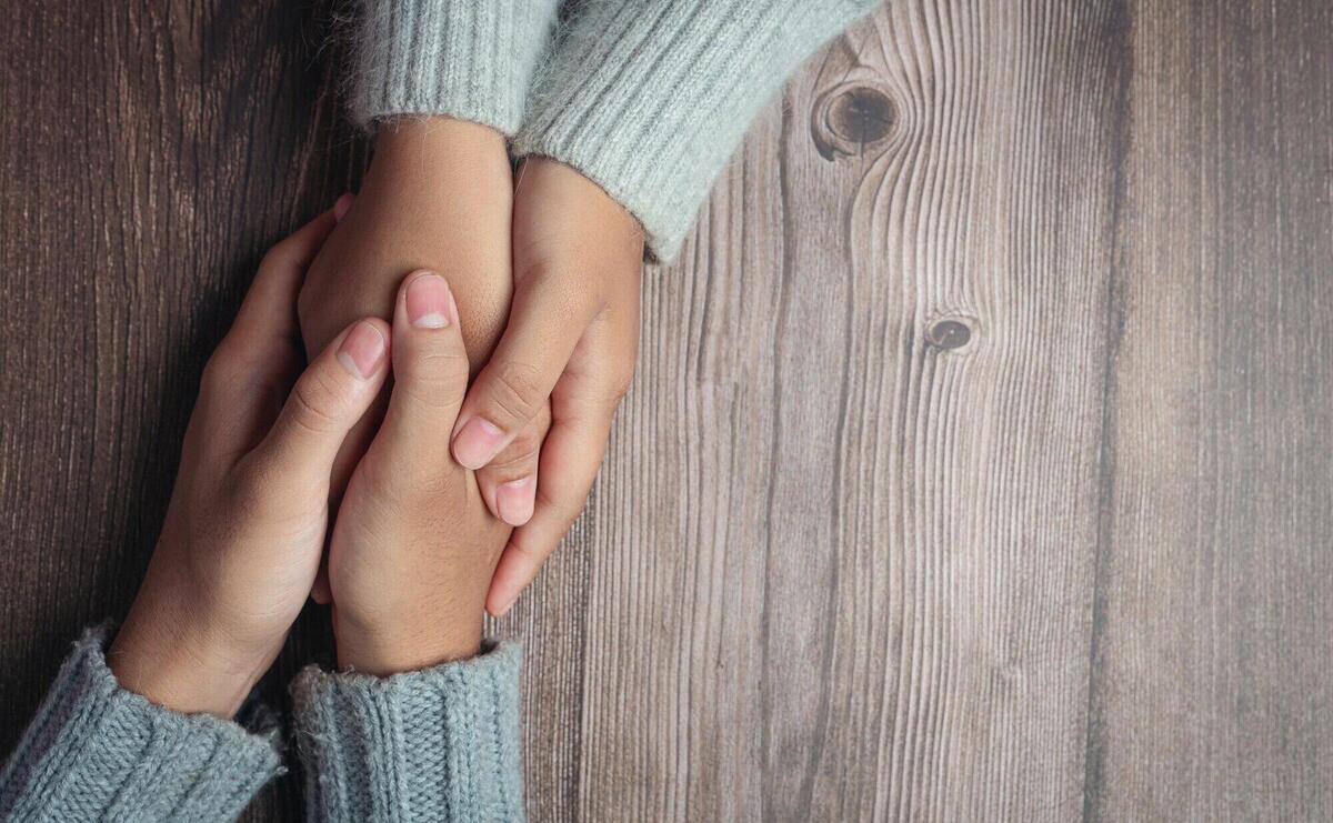 Two people holding hands together with love and warmth on wooden table