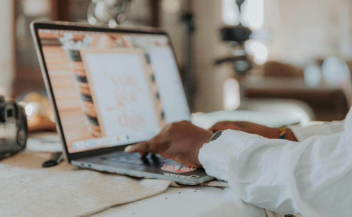 A person typing on a laptop with a blurred screen in a cozy home office setting.