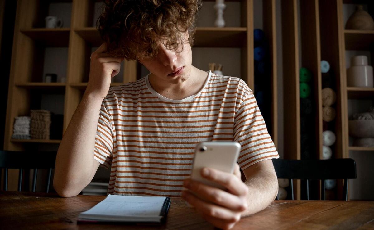 Young man writing something on a notebook while looking at his smartphone