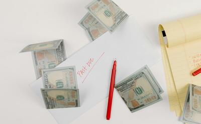 A top-down view of scattered US dollar bills with a 'past due' envelope, red pen, and notepad.