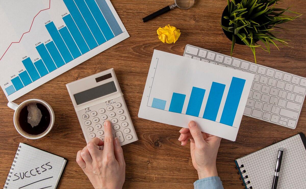 Top view of office desk with growth chart and hands using tiny calculator