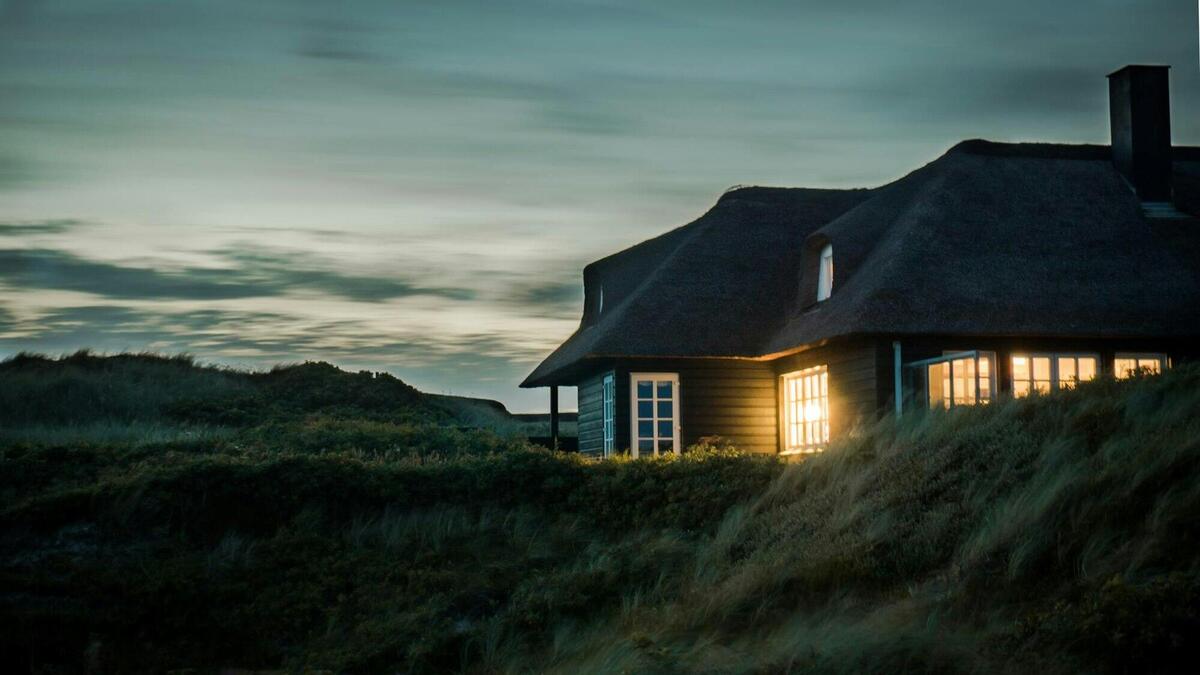 A scenic view of a cozy bungalow illuminated at dusk, nestled in lush greenery.