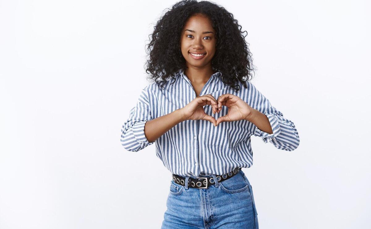 Friendly-looking charming happy young dark-skinned female showing heart gesture romantic love sign smiling broadly feeling sympathy confessing boyfriend heartwarming feelings, relationship concept