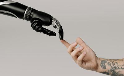 A human hand with tattoos reaching out to a robotic hand on a white background.